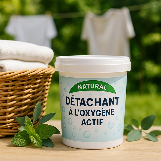 Pot de détachant naturel à l’oxygène actif posé sur une table en bois, entouré de feuilles de menthe et d’eucalyptus, avec un panier en osier rempli de linge blanc à gauche et du linge suspendu en arrière-plan dans un jardin verdoyant.